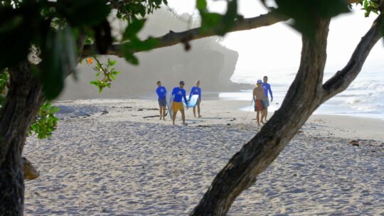 Surfers walking toward the ocean through tropical scenery at Playa La Lancha