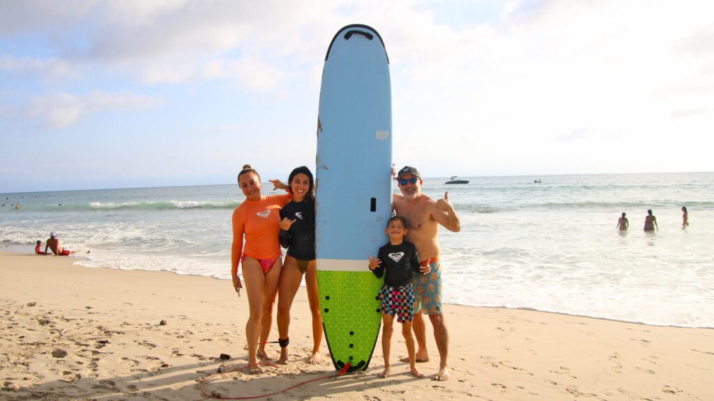 Smiling family posing with surfboard after lesson at La Lancha beach