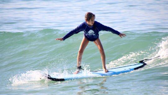 Young girl balancing on a wave at La Lancha beach during her surf lesson