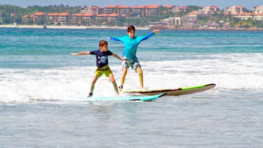 Two kids riding a wave together toward the shore in Punta de Mita