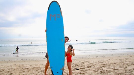 Mother and daughter smiling together with surfboard after a kids surf lesson in Punta Mita