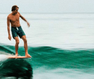 A person practicing yoga on the beach with a surfboard nearby, representing surf fitness and preparation.