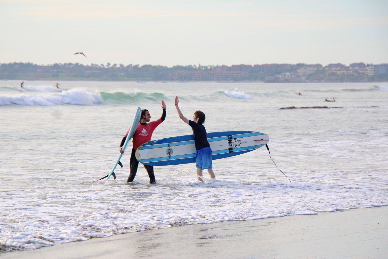 Celebrate progress and connection with our local instructors at La Lancha Teen surfer and Wildmex instructor high-fiving after a surf session at La Lancha beach