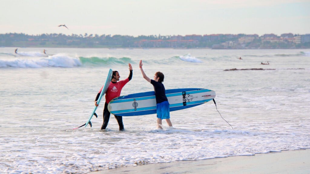 Surf instructor high-fiving a young surfer after a lesson