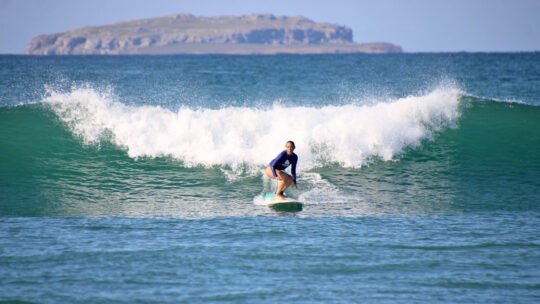 Surfer catching a wave in Punta Mita with Isla Marieta in the background and crystal-clear water
